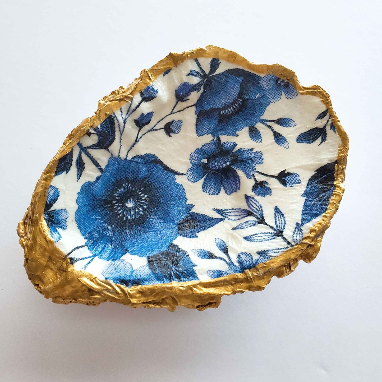 Oyster shell jewelry dish with blue floral design on a white background and gold painted rim