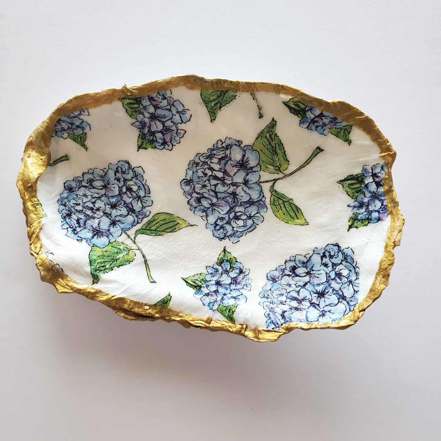 Oyster ring dish with blue hydrangea design on a white background and gold painted rim