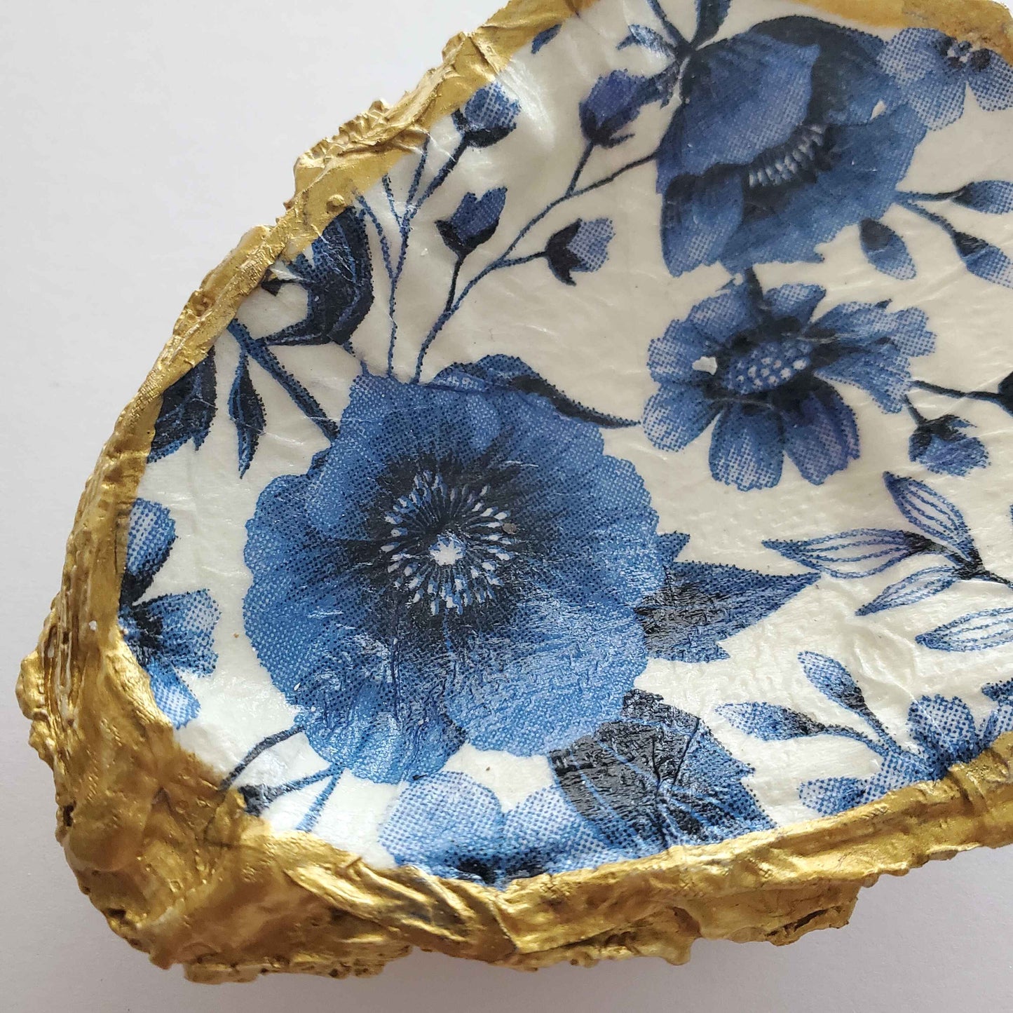 Oyster shell ring dish with a blue floral pattern on a white background and gold painted edges