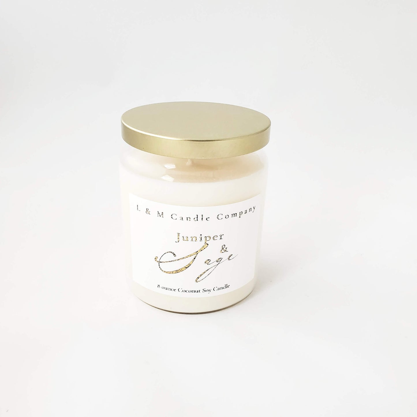 A juniper and sage coconut soy candle by L&M Candle Company hand-poured in a clear glass vintage apothecary vessel and gold lid.