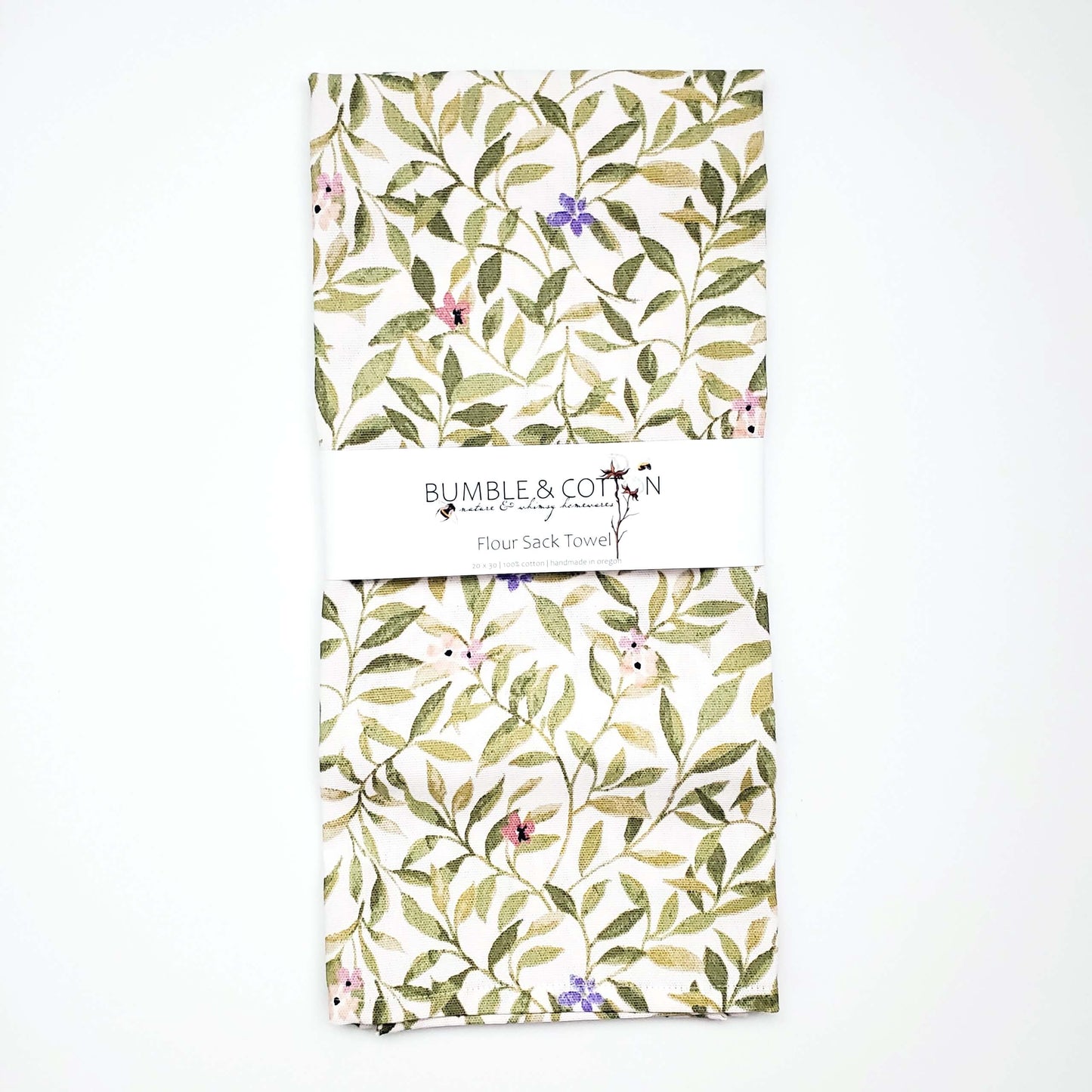 A flour sack towel handmade by Bumble and Cotton featuring a green spring leaves and blossoms print