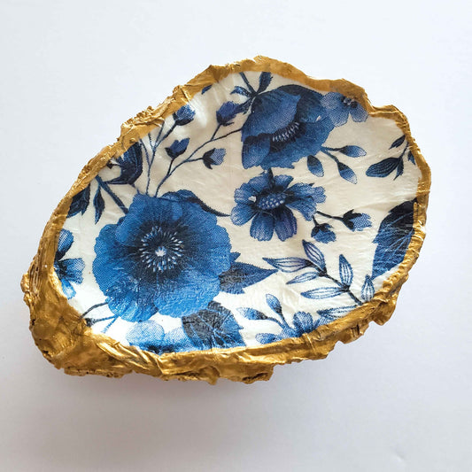 Oyster shell jewelry dish with blue floral design on a white background and gold painted rim
