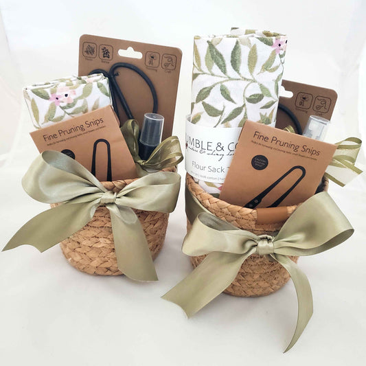Two woven baskets with green ribbons, containing gardening tools and supplies, on a white background.