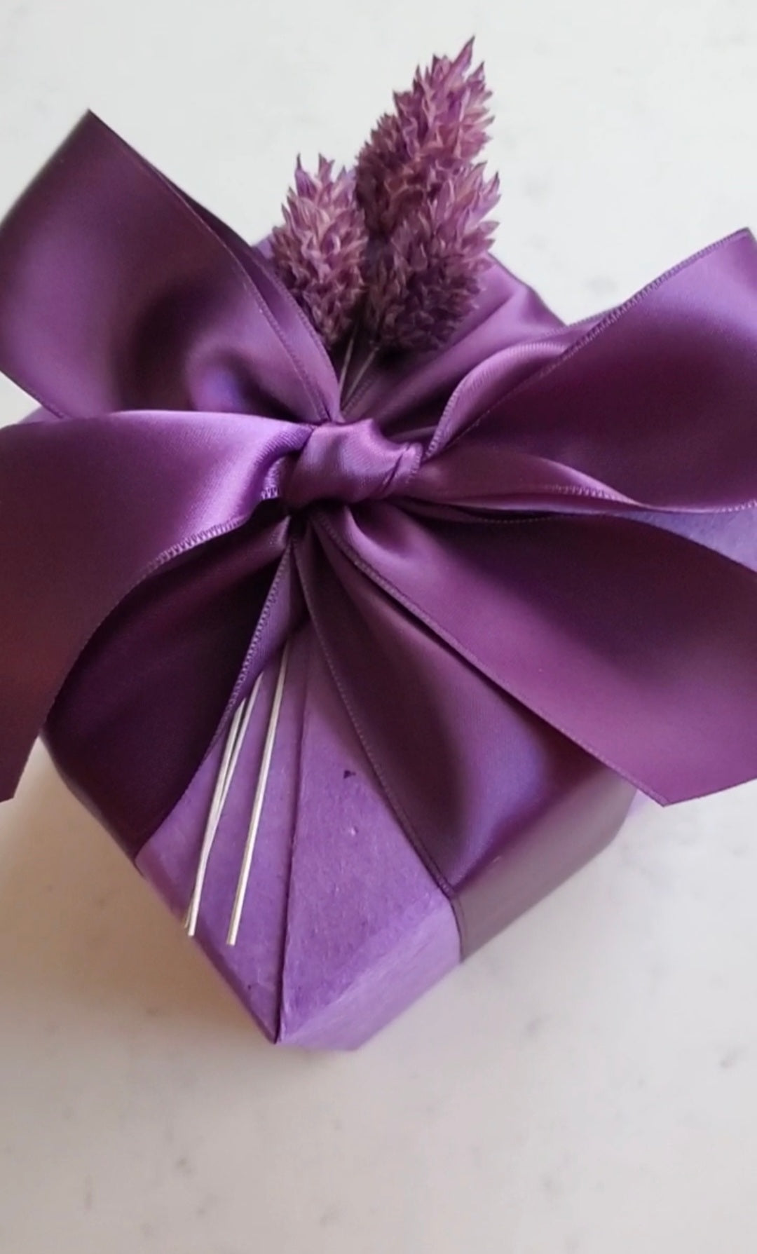 Purple gift box with a large bow and lavender flowers on a light background