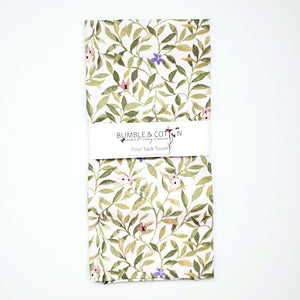 A flour sack towel handmade by Bumble and Cotton featuring a green spring leaves and blossoms print