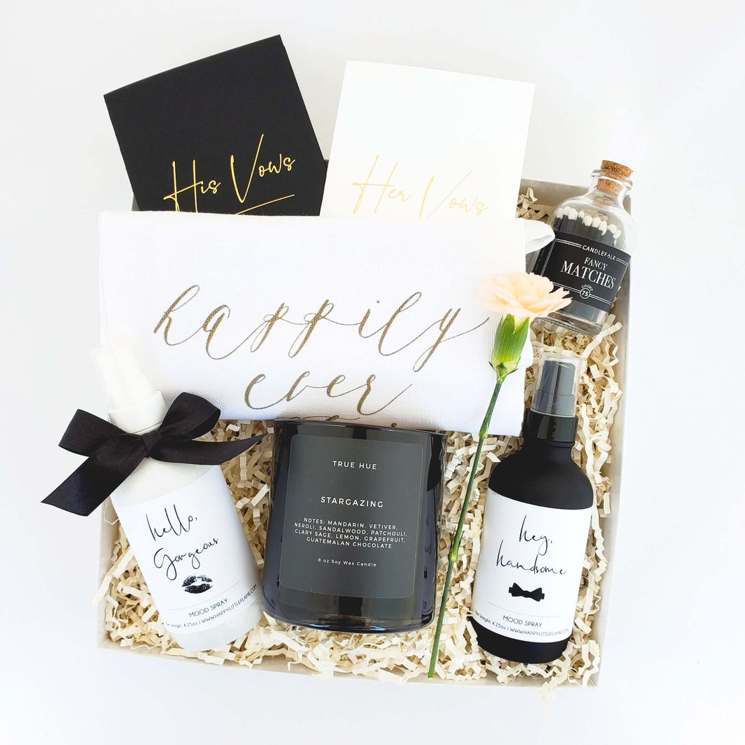 An engagement or wedding gift box with a black and white color palette by The Gift Veil. Includes his and her vow books, a soy candle, black matches, mood sprays and a tea towel that says happily ever after.